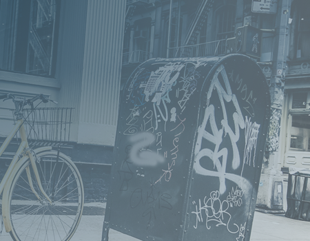 a city street corner with a mailbox covered in graffiti