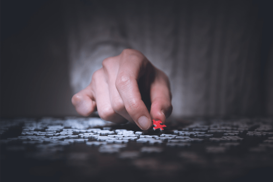 hand putting a red puzzle piece down among white pieces
